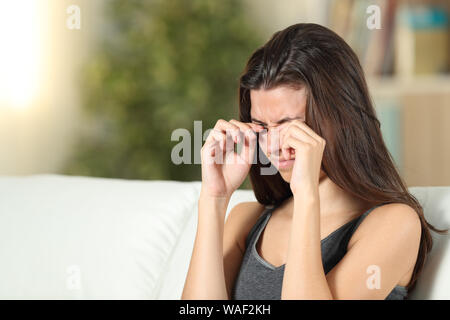 Girl suffering itching scratching eyes sitting on a couch in the living room at home Stock Photo