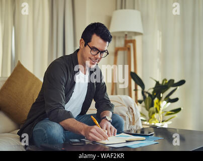 Happy man writing on notebook with pen at home Stock Photo