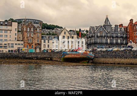 Oban, United Kingdom - February 20, 2010: bay with houses on grey sky. City architecture along sea quay. Resort town with hotels. Summer vacation on island. Travelling and wanderlust. Stock Photo