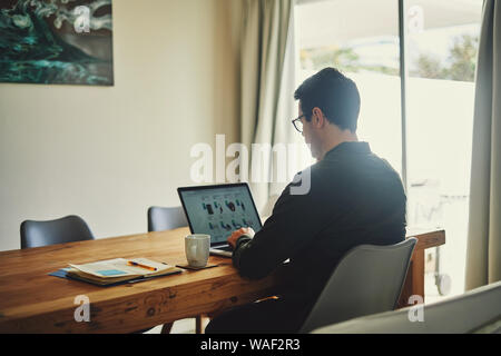 Man sitting near window busy using laptop at desk Stock Photo