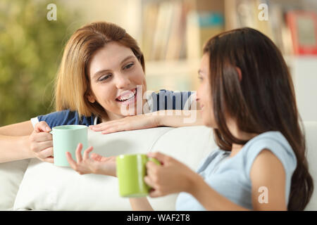 Happy friends talking at home drinking coffee sitting on a couch in the living room at home Stock Photo