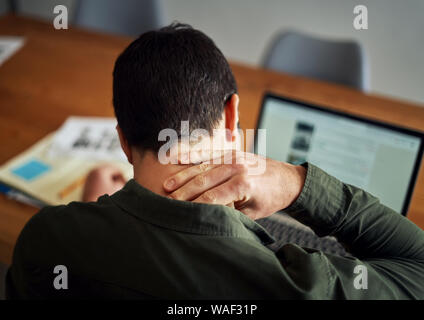 Man suffering from neck pain while working on laptop Stock Photo
