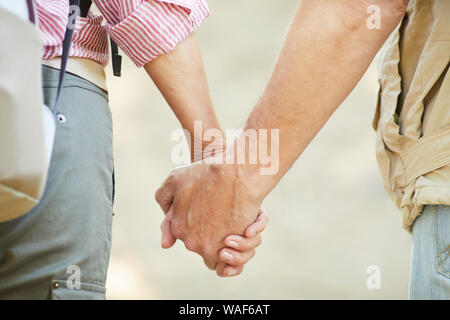 Close-up of mature couple holding hands and walking together outdoors in summer day Stock Photo