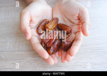 hand holding dried fruits from date palm on wooden background, phoenix dactylifera in hand. Stock Photo