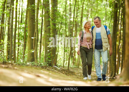 Senior happy couple embracing each other and walking along the footpath during their hike in the forest in summer day Stock Photo