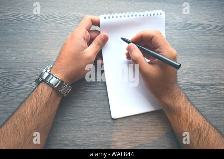 Man writing in a notebook.High angle view of man hand writing on wooden desk. Making notes, close up.Top view man hands with metal silver watches Stock Photo