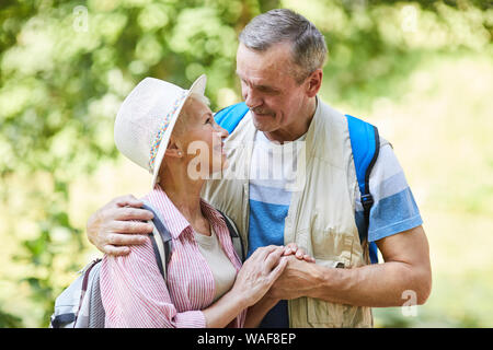 Senior happy couple hiking in the forest they standing holding hands and looking at each other with tender Stock Photo