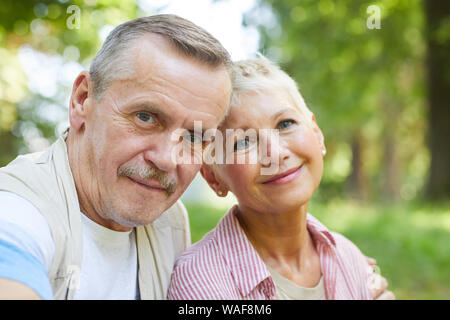 Portrait of beautiful mature couple smiling at camera while spending time together on fresh air in the park Stock Photo