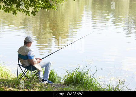 Mature man sitting on chair with fishing rod and fishing near the pond in  nature Stock Photo - Alamy