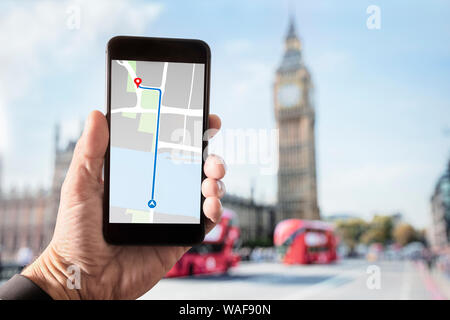 Hand holding smartphone with map on screen in London in front of Big Ben and Houses of Parliament on Westminster Bridge Stock Photo