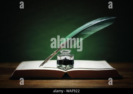 Quill pen and inkwell resting on an old book with green background concept for literature, writing, author and history Stock Photo