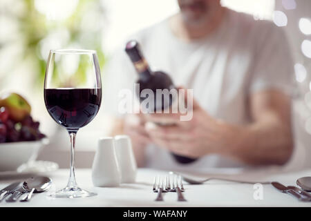 Man reading red wine bottle label in restaurant focus on glass Stock Photo
