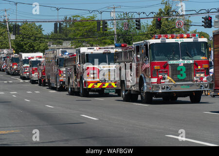 Long Island, NY - Circa 2019: Memorial day parade celebration down closed road. Spectators watch fire department truck brigade drive by with sirens an Stock Photo