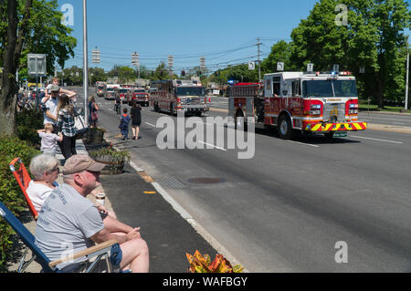 Long Island, NY - Circa 2019: Memorial day parade celebration down closed road. Spectators watch fire truck brigade drive by with sirens and horns to Stock Photo