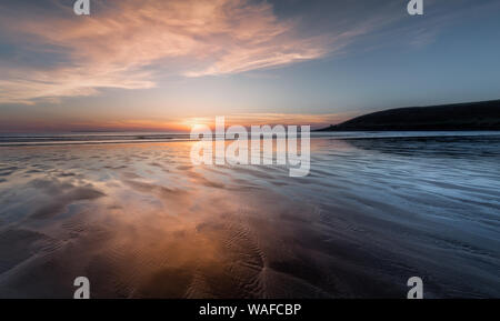 Sun dipping on the horizon, at the beautiful Saunton Sands on the  North Devon coast, at Low Tide. Stock Photo