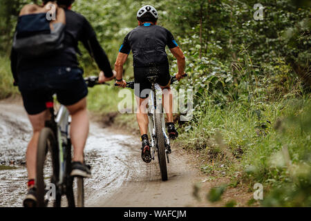 back two cyclists riding mountain bike on dirty trail in forest Stock Photo