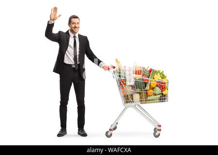 Full length portrait of a businessman with a shopping cart full of food products waving at the camera isolated on white background Stock Photo