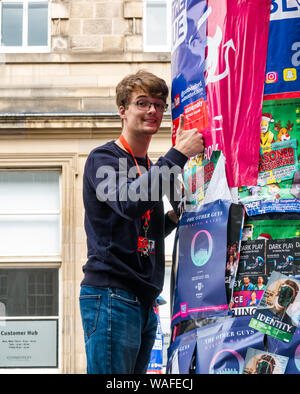 Edinburgh, Scotland, UK, 20 August 2019. Edinburgh Festival Fringe: Performers on the Royal Mile try to attract people to their shows by sticking posters on an advertising column Stock Photo