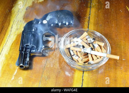 revolver gun and cigarette in glass ashtray on wooden table Stock Photo
