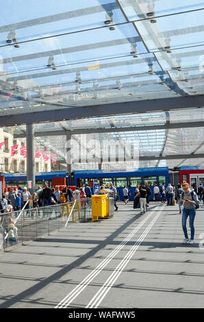 Bern, Switzerland - August 14 2019: People walking under the roof by tram station. The station is adjacent to the main train station. Tram in background. Public transport. Daily life. Swiss capital. Stock Photo