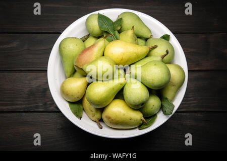 Fresh organic pears in bowl on dark wooden table. Top view Stock Photo