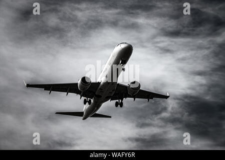 Airplane landing in front of dramatic sky in black and white Stock Photo