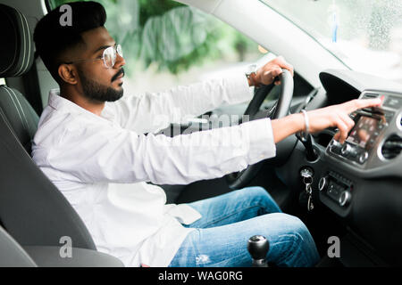 Presses the stop. Young indian man hitting car emergency red light button in the cars. Stock Photo