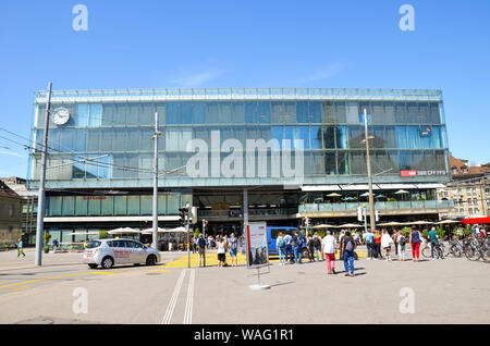 Bern, Switzerland - August 14 2019: Building of the main train station in Swiss capital photographed from outside with people waiting on adjacent zebra crossing. Daily life. Public transport. Stock Photo