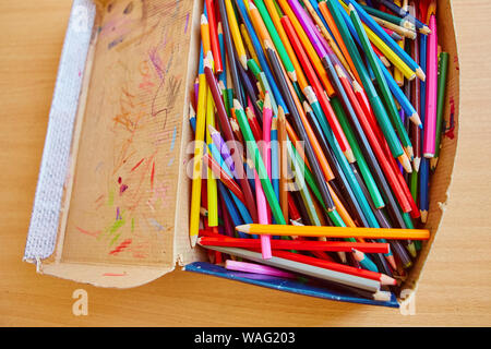 Lots of old colored wooden pencils in a cardboard box with children's doodles. Stock Photo