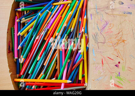 Lots of old colored wooden pencils in a cardboard box with children's doodles. Stock Photo