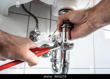 man repairing sink trap with adjustable pipe wrench in bathroom Stock Photo