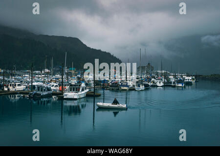 Long man in boat sails into Whittier harbor on a rainy day Stock Photo