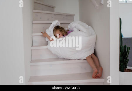 young blonde girl playing wrapped up in a duvet cover on the stairs Stock Photo
