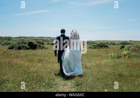 bride and groom walking through a field of green on their wedding day Stock Photo