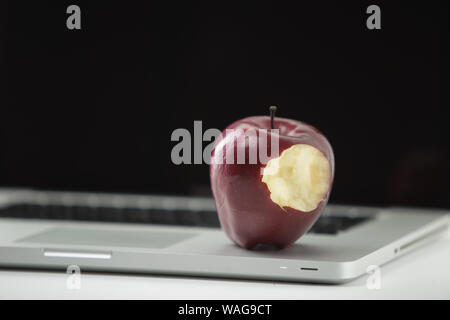 Shiny red apple resting on an open aluminum laptop in selective focus on white background Stock Photo