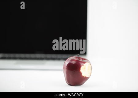 Shiny red apple resting on an open aluminum laptop in selective focus on white background Stock Photo
