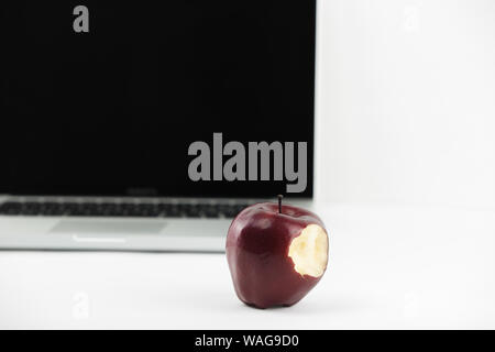 Shiny red apple resting on an open aluminum laptop in selective focus on white background Stock Photo