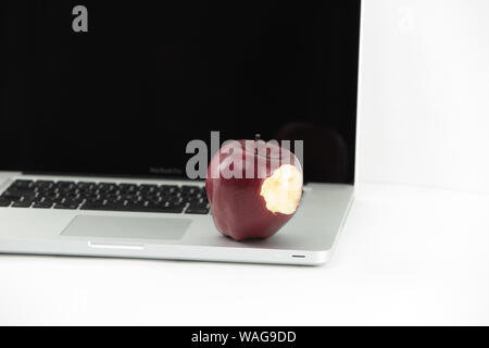 Shiny red apple resting on an open aluminum laptop in selective focus on white background Stock Photo
