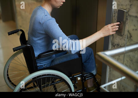 Close-up of young disabled female patient in wheelchair pushing the button and using the elevator Stock Photo