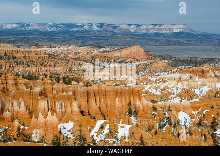 Sun lit Bryce Canyon in detailed (still broad) view. Red / ochre canyon rock formations in places overgrown by green pines, partly covered by snow Stock Photo
