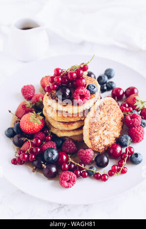 Cottage cheese pancakes served with lots of fresh berries on white background. Gourmet Breakfast - Cottage cheese syrniki, curd fritters with raspberr Stock Photo