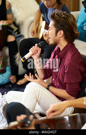 young asian adult men rock band members rehearsing singing playing musical instruments in living room of a house Stock Photo