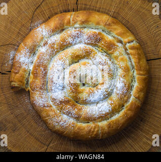 Round apple pie on a wooden rustic background. Homemade Organic Apple Pie with icing sugar or Burek. Top view photo of tasty apple pie with sugar. Stock Photo