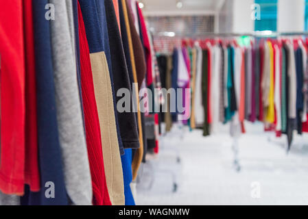 Close up view row of colourful tone of knitted crocheted sweater and jumper hang on aluminium hanger clothes rack in retail fashion store. Stock Photo