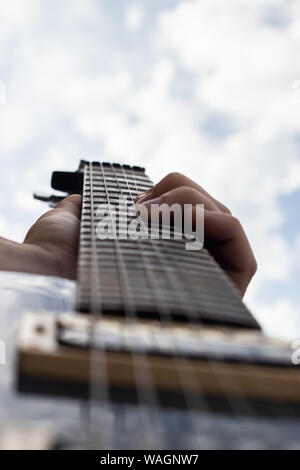 Male hand playing electric guitar and bending the strings with blue cloudy sky in the background Stock Photo