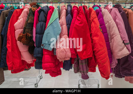 Row of colourful red and pink tone of kid winter jackets hang on aluminium hanger clothes rack in retail fashion store or second hand outlet shop. Stock Photo