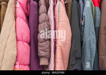 Row of colourful red and pink tone of kid winter jackets hang on aluminium hanger clothes rack in retail fashion store or second hand outlet shop. Stock Photo