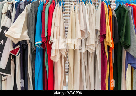 Row of colourful tone and white of T-shirts hang on aluminium hanger clothes rack in retail fashion store or second hand outlet shop. Stock Photo