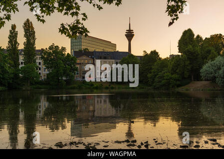 Outdoor silhouette view with twilight sky at Ständehaus park with reflection in the lake, and background of buildings and Rhine tower. Stock Photo