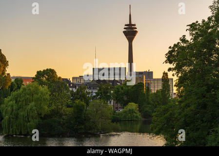 Outdoor silhouette view with twilight sky at Ständehaus park with reflection in the lake, and background of buildings and Rhine tower. Stock Photo